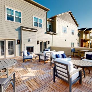 A spacious outdoor deck area with comfortable seating and tables, attached to a residential building.