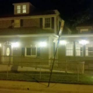 A house illuminated by soft lights at night, with a utility pole leaning precariously nearby.