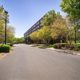 A road alongside a multi-story building surrounded by trees and greenery.