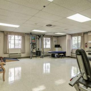 A spacious fitness room with various gym equipment, including a treadmill and a ping pong table, under bright lighting.