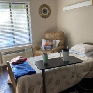 A cozy hospital room with a bed, reclining chair, and a window letting in daylight.