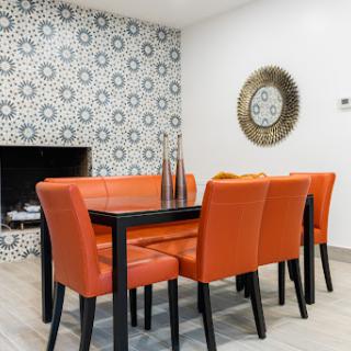 A stylish dining room featuring vibrant orange chairs and a black table, complemented by a decorative wall and contemporary decor.