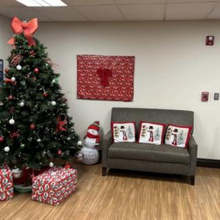 A cozy corner decorated for the holidays with a Christmas tree, festive pillows on a couch, and wrapped gifts.