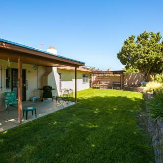 A cozy backyard with a grassy lawn, patio, and outdoor seating under a clear blue sky.