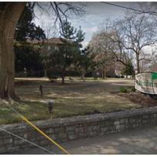 A serene park setting bordered by a stone wall, featuring trees and grass, with a construction trailer in the background.