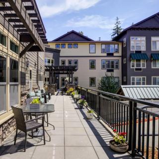A modern apartment complex with a spacious balcony featuring outdoor seating and plants, under a clear blue sky.