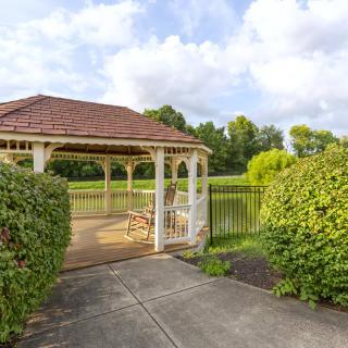 A serene gazebo overlooking a pond in a park setting, surrounded by lush greenery.