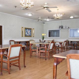 A spacious dining area featuring wooden tables and chairs, adorned with chandeliers and ceiling fans.