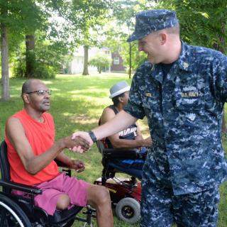 A military personnel shaking hands with a person in a wheelchair outdoors.
