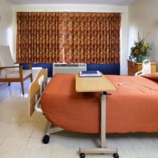 A hospital room with a bed, side table, and curtain-covered window.