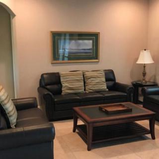 A cozy living room featuring a black leather sofa set, coffee table, lamp, and framed wall art.