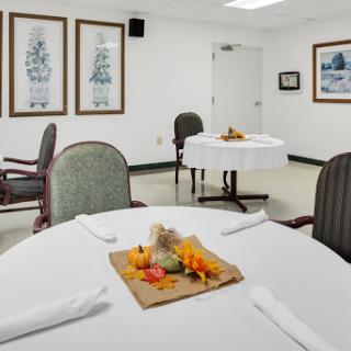 A well-lit dining room featuring a round table with autumn-themed decor and framed artwork on the walls.