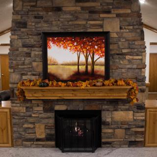 A cozy fireplace adorned with autumn leaves and a beautiful painting of trees in fall colors.