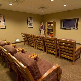 A waiting room with rows of wooden chairs arranged in front of a television.