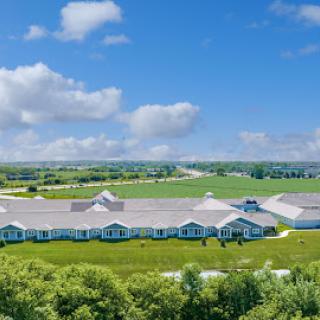 Aerial view of a large building surrounded by lush green fields and a bright blue sky.