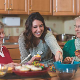 A caregiver shares a joyful moment with elderly individuals while preparing desserts in the kitchen.