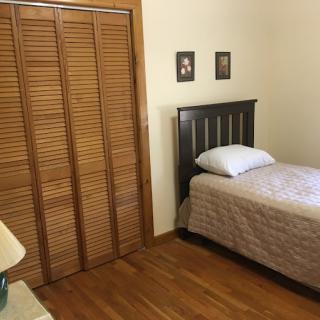 A cozy bedroom with a single bed, wooden floor, and a closet.