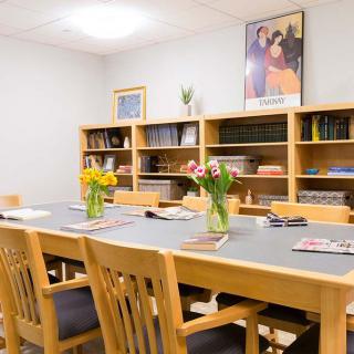 A well-lit conference room with a large table, surrounded by wooden chairs and lined with bookshelves. The table is adorned with vases of fresh flowers.