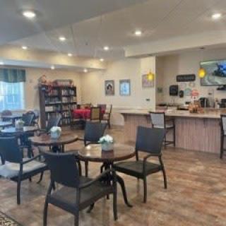 A cozy cafe interior with tables, chairs, a bookshelf, and a coffee station.