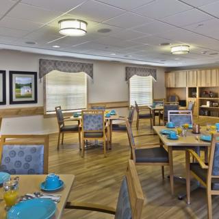 An inviting dining room with tables and chairs neatly arranged, featuring blue dishware and warm lighting.