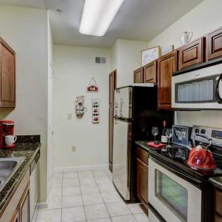 A compact kitchen with wooden cabinets, appliances including a microwave, oven, and fridge, along with tiled flooring.