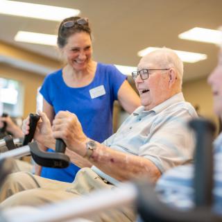 An elderly man exercising in a gym with assistance from a trainer.