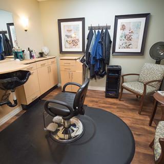 A cozy barber shop interior with a single haircut station, featuring a chair, mirror, and various decor elements.