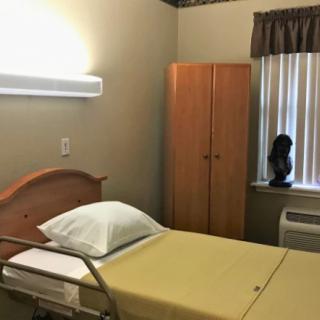 A hospital room featuring a bed, wardrobe, and a window with curtains.