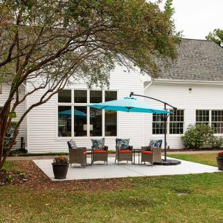 A cozy backyard patio setup with chairs under a blue umbrella beside a white house.