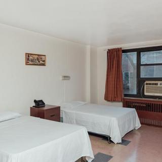 A simple bedroom with two single beds, white sheets, a nightstand, and an air conditioner by the window.