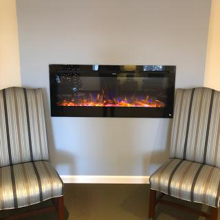A cozy electric fireplace set in a wall, flanked by two striped chairs.