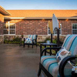 A cozy patio area with cushioned chairs against a brick building during sunset.
