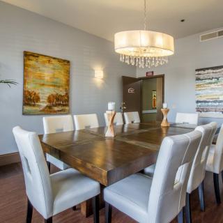 A stylish dining room featuring a large wooden table surrounded by white chairs, with a modern chandelier overhead and wall art decorating the space.
