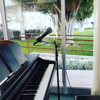 A piano set up for a musical performance, accompanied by a microphone and a view of lush greenery outside.