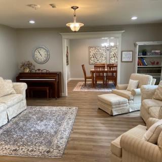 A cozy living room with comfortable seating, a piano, and a view into the dining area.