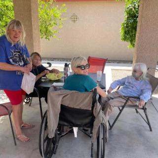A group of people enjoying a sunny day outdoors, with caregivers attending to elderly individuals.