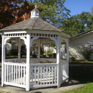 A white wooden gazebo in a garden setting.