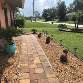 A landscaped front yard featuring a paved pathway surrounded by pebbles and plants.