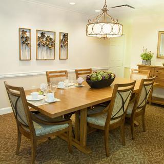A well-lit dining room with a wooden table and chairs, featuring a chandelier and decorative wall art.