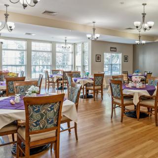 A well-decorated dining room with multiple tables set up, featuring hardwood flooring and large windows.