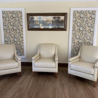 A cozy living room setup featuring three beige armchairs, decorative wall art, and a wooden floor.
