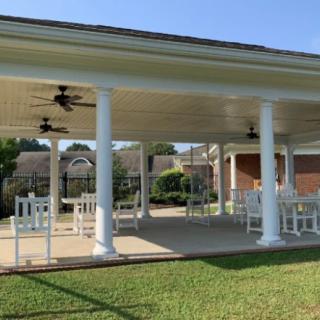 A spacious outdoor pavilion with seating and ceiling fans, surrounded by a garden.