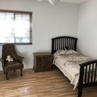 A simple bedroom with a single wooden bed, nightstand, and chair on a wooden floor.