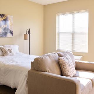 A cozy and bright bedroom featuring a comfortable bed, a stylish sofa, and natural light coming through the window.