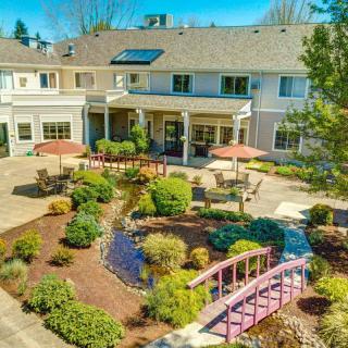 A beautifully landscaped garden with a small bridge and patio area in front of a large residential building on a sunny day.