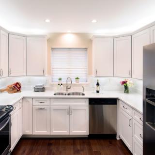A modern kitchen with white cabinets, stainless steel appliances, and hardwood flooring.