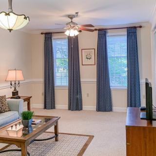 A cozy living room with a sofa, coffee table, lamps, and a television, featuring blue curtains and warm lighting.