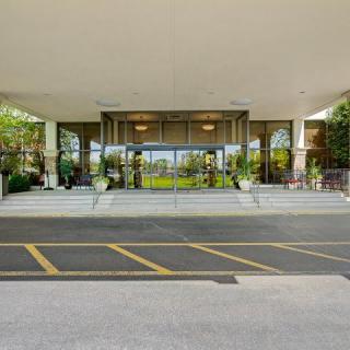 The entrance features glass doors, front steps, and potted plants beneath a large awning.