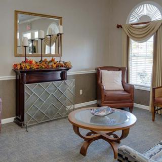 A cozy living room with elegant furnishings, featuring an armchair, a small round table, and a decorative mirror above a mantelpiece.