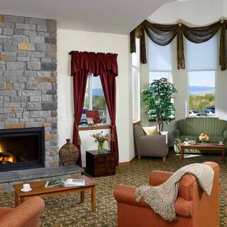 A cozy living room with a stone fireplace, comfortable armchairs, and large windows showcasing an inviting view.